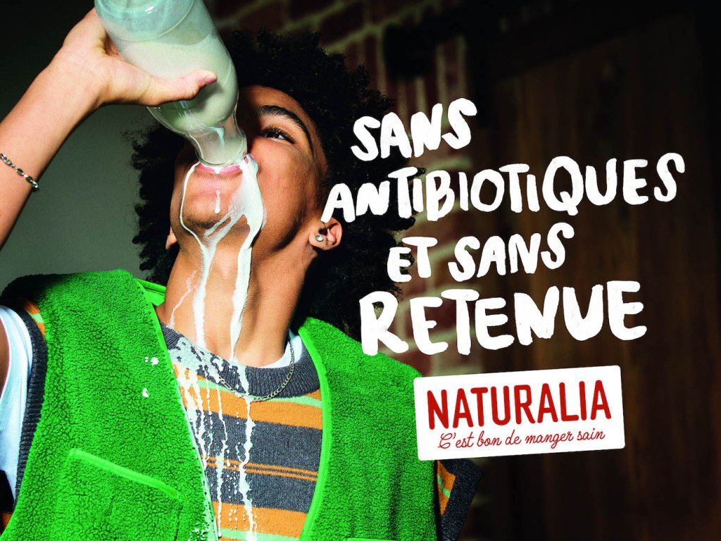 Publicité Naturalia - C'est bon de manger sain - Agence Altmann+Pacreau - 2023 - Sans antibiotiques et sans retenue - Jeune homme boit avidement au goulot d'une bouteille de lait