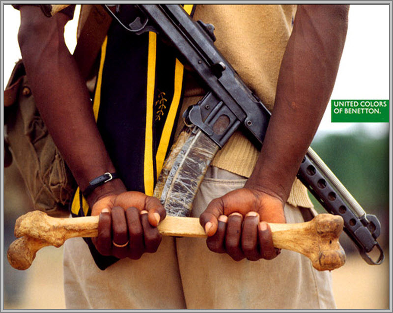 Publicité Benetton - United colors of Benetton — Oliviero Toscani - Un homme avec un kalachnikov tenant mains dans le dos un fémur - 1992