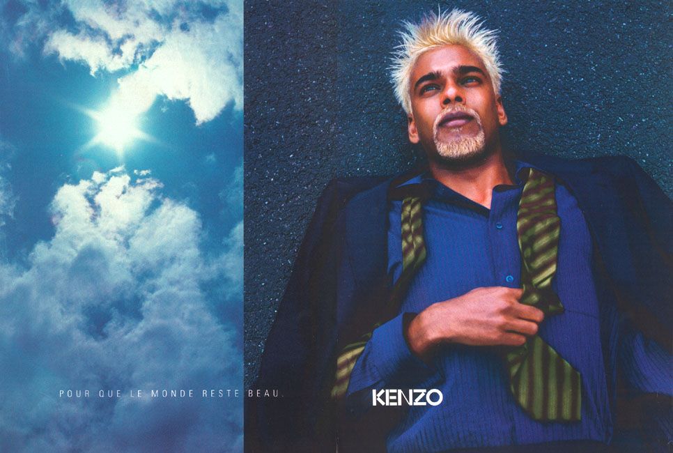 Publicité Kenzo - Pour que le monde reste beau - Prêt à porter 1998 - Homme en costume allongé sur du bitume - Ciel nuageux en vis-à-vis 