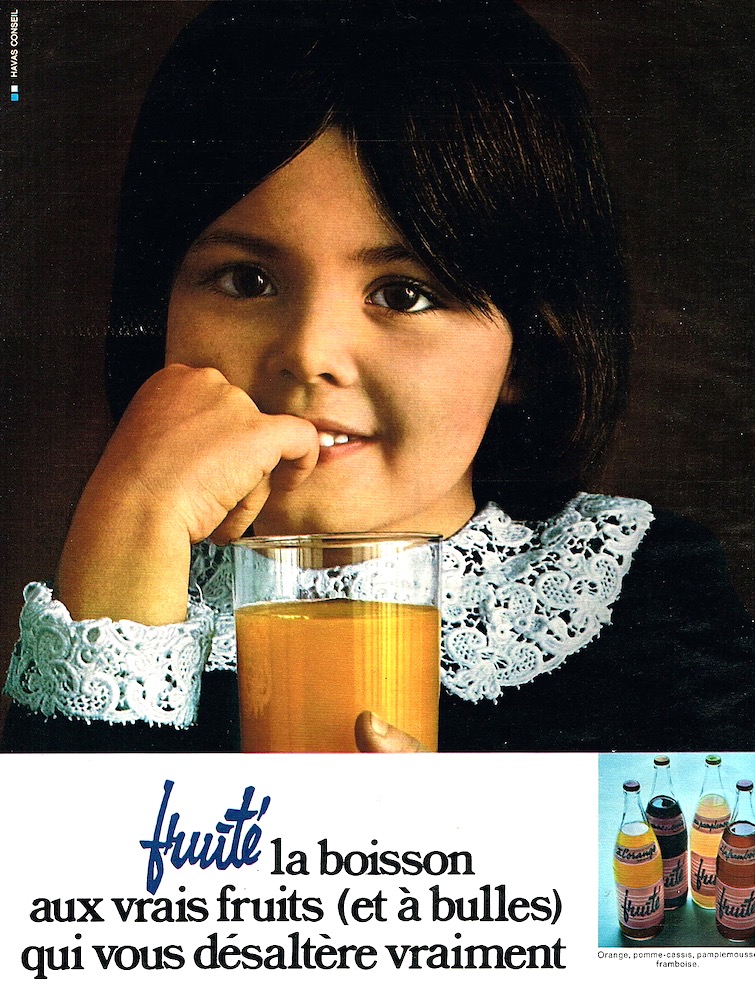Publicité evian Fruité - Fruité, la boisson aux vrais fruits (et à bulles) qui vous désaltère vraiment - Gros plan d'une fillette avec un verre devant elle - 1970