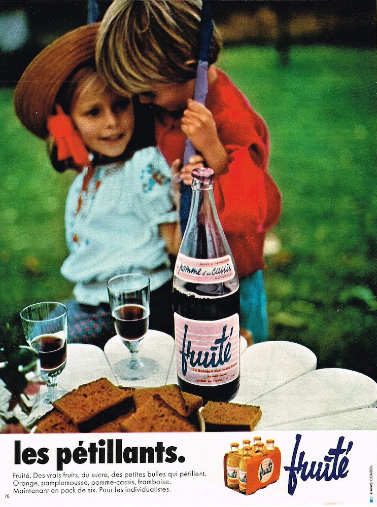 Publicité evian Fruité - Les pétillants - Un couple d'enfants devant une table de jardin avec deux verres, une bouteille et du pain d'épice - 1971