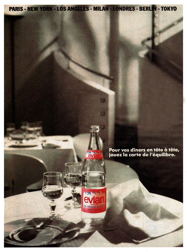 Publicité evian - Pour vos dîners en tête-à-tête, jouez la carte de l'équilibre - Bouteille en couleur au milieu d'un décor de restaurant en noir et blanc - 1988