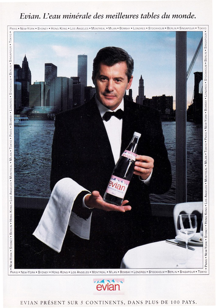 Publicité evian - L'eau minérale des meilleures tables du monde - Un serveur présente la bouteille en verre devant un décor new-yorkais - Évian présent sur 5 continents, dans plus de 100 pays - Agence Eurocom - 1993