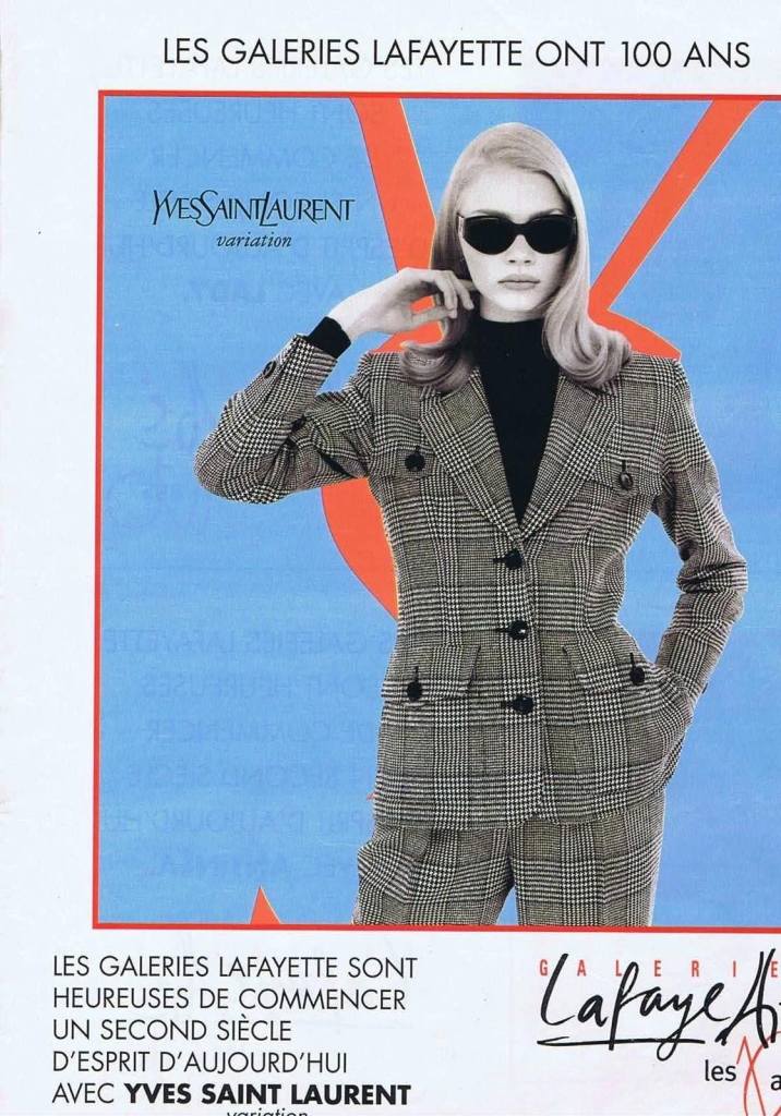 Publicité Galeries Lafayette - Les Galeries Lafayette ont 100 ans - Yves St Laurent - Femme en tailleur noir et blanc devant logo en orange sur fond bleu - 1996