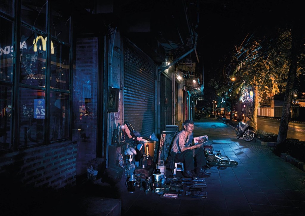 Publicité McDonald's - 24/24h - Reflets - Un marchand de rue lit un magazine - Le logo de la marque se reflète sur la devanture d'un magasin - TBWA/DANThailand - Thaïlande - 2017