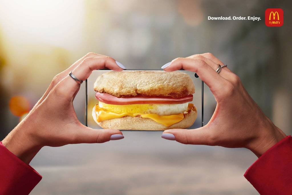Publicité McDonald's - Application - Download.Order.Enjoy - Deux mains tiennent un téléphone comme si elle tenait un Egg Muffin, qui apparait sur celui-ci - Agence Cossette - Canada - 2020