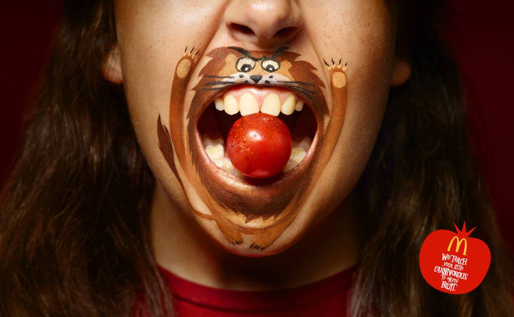 Publicité McDonald's - We teach your little carnivorous to enjoy fruit/Vegetable - Fillette avec un maquillage de lion autour de la bouche a une mini tomate entre ses dents - Agence TBWA - Espagne - 2018
